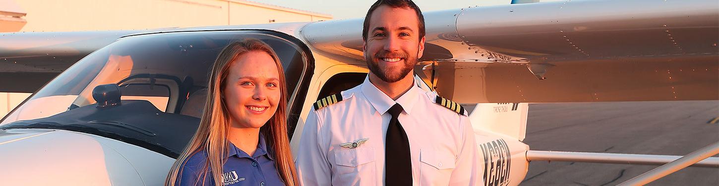 Two people pose for a photo outside of a small aircraft