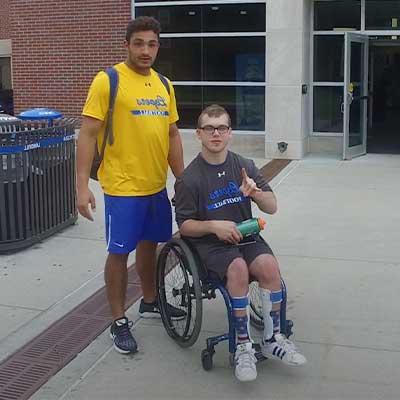 一名学生站在另一名使用轮椅的学生旁边